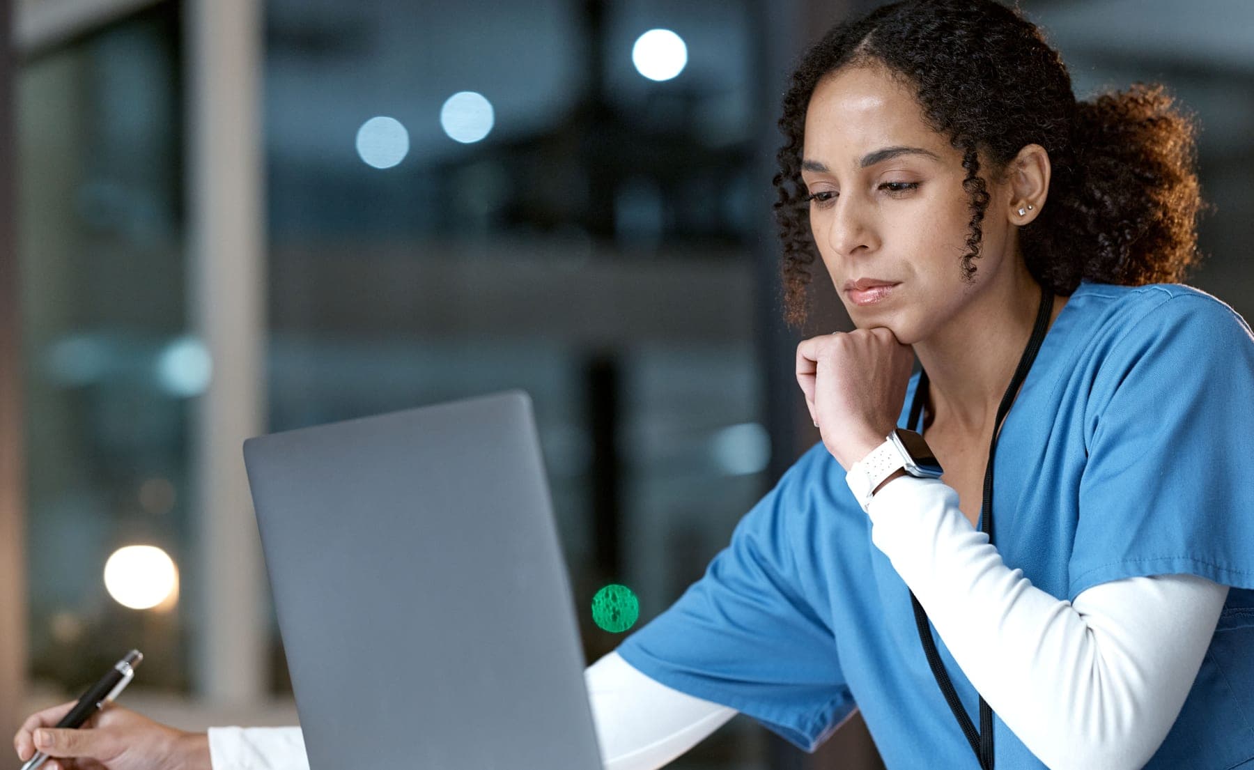 A nurse working at a laptop while reviewing notes, representing the balance between clinical judgment and technology.