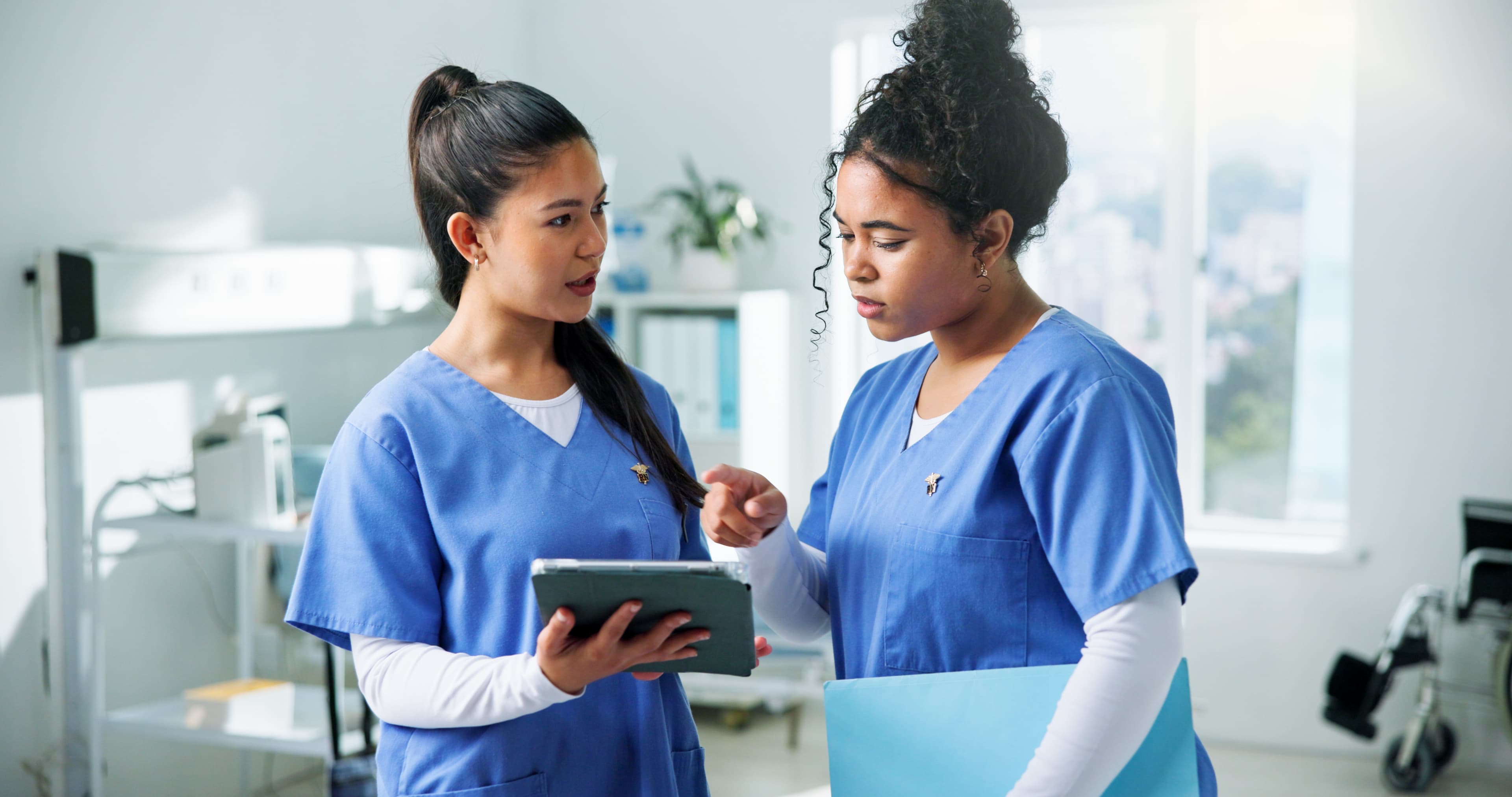 Two nurses reviewing information on a tablet together in a hospital setting. Licensed illustrative stock photograph, not a CEC client.